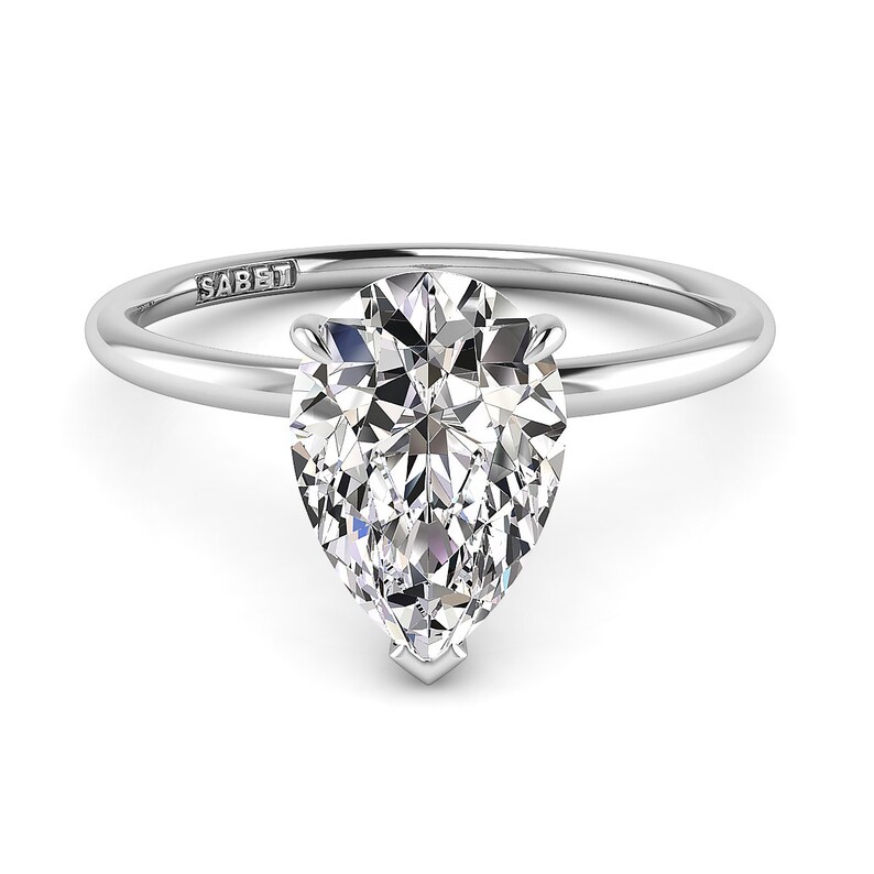 Puede incluir: Un anillo de compromiso de plata con un diamante de forma de pera. El anillo est&aacute; grabado con la palabra "SABET".