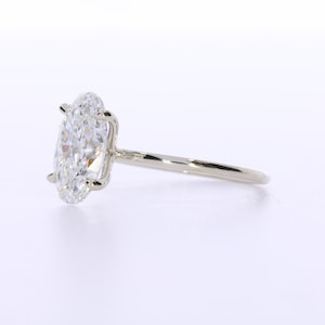 May include: A solitaire engagement ring with a large, oval-cut diamond. The diamond is set in a four-prong setting on a thin, polished silver band. The ring is displayed on a white background.