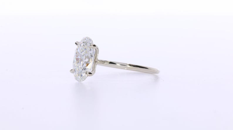 May include: A solitaire engagement ring with a large, oval-cut diamond. The diamond is set in a four-prong setting on a thin, polished silver band. The ring is displayed on a white background.