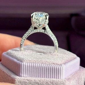 Può includere: Un anello color argento con una grande pietra centrale dal taglio ovale fissata con griffe. Il gambo e la montatura che circonda la pietra centrale sono incastonati con numerose piccole pietre trasparenti dal taglio rotondo che riflettono la luce.
