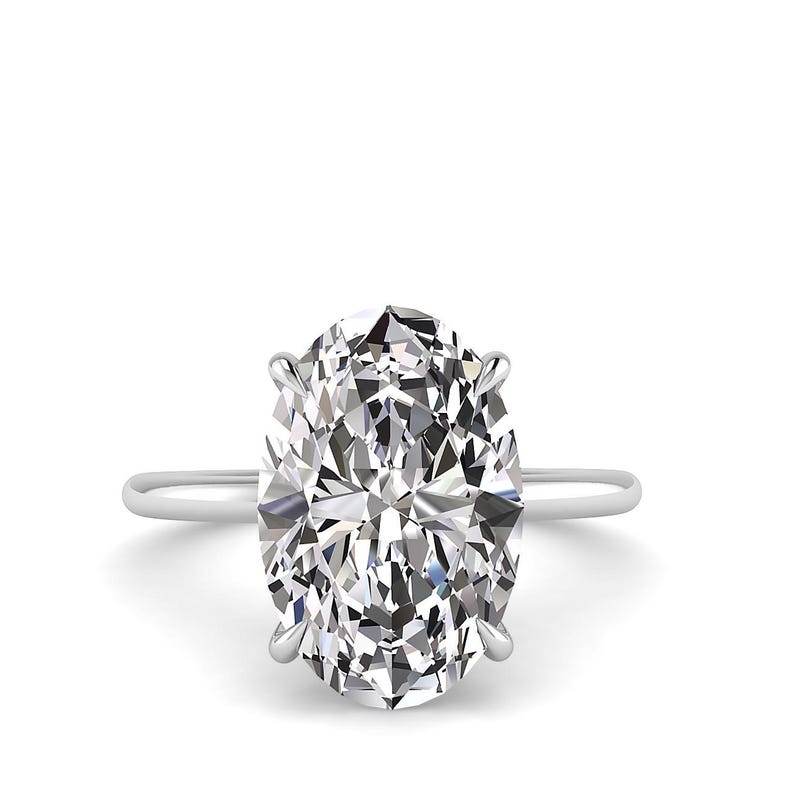May include: A solitaire engagement ring featuring a large, oval-cut diamond. The diamond is set in a simple, thin, silver band. The gemstone sparkles with many facets, reflecting light. The ring is set against a white background.