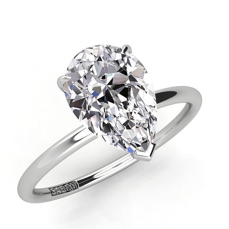 Puede incluir: Un anillo de compromiso de diamante en forma de pera engastado en una banda de plata. El anillo est&aacute; grabado con la palabra "SABERI".