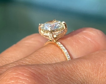 May include: A gold engagement ring with a large oval-shaped diamond center stone and a halo of smaller diamonds. The band is also set with smaller diamonds.