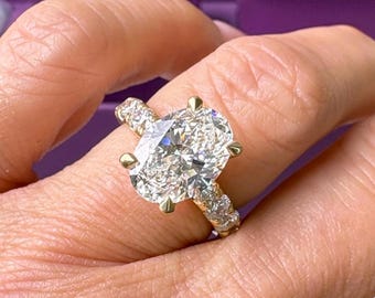 May include: A gold ring featuring a large, oval-cut center stone held by four prongs. The band is adorned with a series of smaller, round-cut stones set along the sides, creating a continuous sparkling effect across the visible portion of the ring.