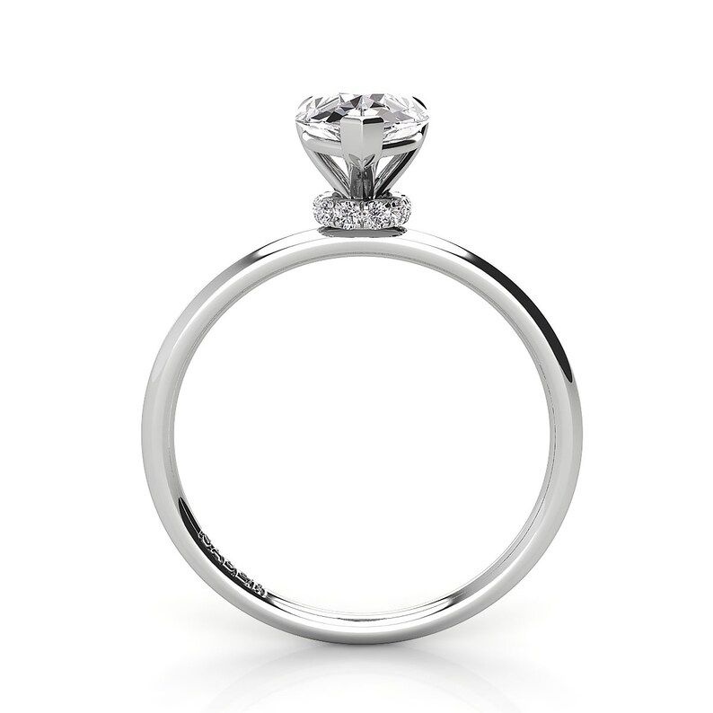 Puede incluir: Un anillo de compromiso de plata con una piedra central redonda y clara y una banda de diamantes m&aacute;s peque&ntilde;os alrededor de la base del engaste.