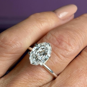 Puede incluir: Un anillo de diamantes con corte marquesa y un halo de diamantes más pequeños. El anillo tiene una banda plateada.