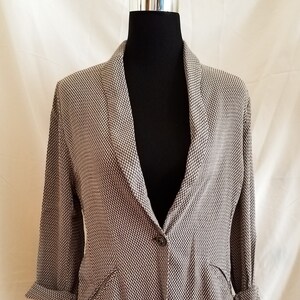 Puede incluir: Una chaqueta de punto marrón y blanco con un cierre de botón único y mangas largas. La chaqueta tiene un cuello y dos bolsillos.