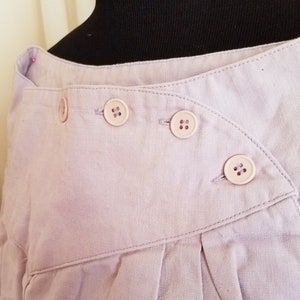 May include: A lavender linen skirt with a diagonal fold and three button closures.
