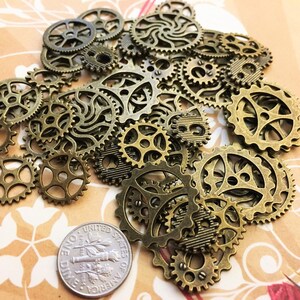 May include: A collection of antique gold-toned metal gears of various sizes. The gears are arranged in a pile on a brown surface.