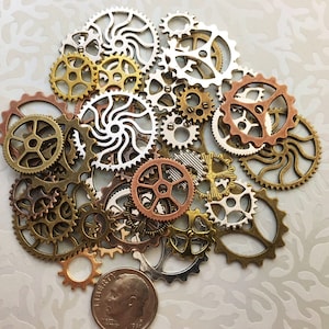 May include: A collection of gold, silver, and copper-toned metal gears and cogs, some with a swirl design, arranged in a circular pattern on a white background.