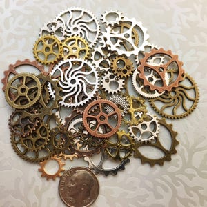 May include: A collection of various sized metal gears in shades of silver, gold, bronze, and copper. The gears are arranged in a pile, with a dime for size comparison. The gears have intricate designs and are likely for crafting or steampunk projects.