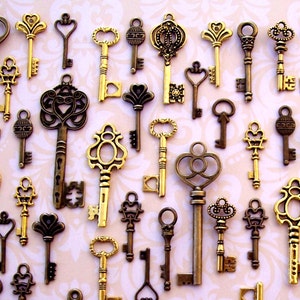 May include: An assortment of antique-style keys in various sizes and designs. The keys are primarily gold and bronze in color, with ornate details and decorative key heads. The keys are arranged on a light pink and white patterned background.