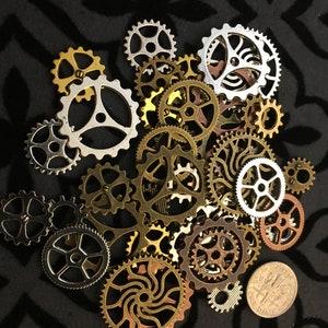 May include: A collection of assorted metal gears in gold, silver, and copper tones. The gears are arranged in a random pattern on a black background.