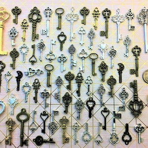 May include: A collection of assorted metal skeleton key charms in various finishes including gold, silver, bronze, and black. The keys feature intricate filigree, heart-shaped bows, and ornate patterns. A U.S. dime is included for scale reference.