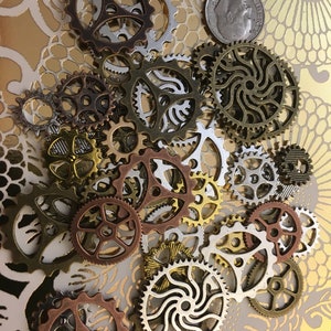 May include: A collection of assorted metal gear and cog components in various finishes including copper, brass, silver, and bronze. A United States dime is included for scale, measuring approximately 0.7 inches in diameter, to show the size of the gears.