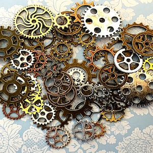 May include: A collection of various sized metal gears in shades of gold, bronze, and silver. The gears are arranged in a cluster, showcasing different designs and textures. The background is a light blue floral pattern.
