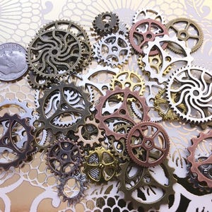 May include: A collection of various-sized metal gears in bronze, copper, silver, and gold tones. A U.S. dime is included for size comparison. The gears have intricate designs and are arranged on a gold floral patterned background.