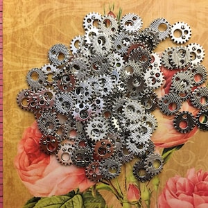 May include: A large pile of silver metal gears of various sizes and shapes. The gears are scattered on a background of pink and brown floral fabric.
