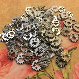May include: A pile of silver metal gears, some with a gold finish, scattered on a floral patterned surface. The gears are various sizes and shapes.