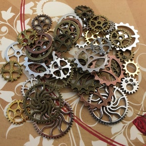 May include: A collection of assorted metal gear charms in various sizes and designs, featuring metallic finishes in silver, gold, copper, and bronze tones. These small, circular mechanical components have intricate cut-out patterns and teeth.