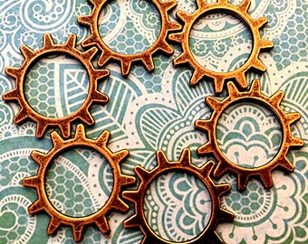 May include: Five copper-colored metal gears with a decorative, ornate design. The gears are arranged in a circular pattern on a blue and white patterned background.