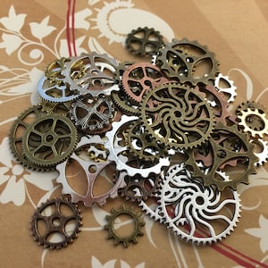 May include: A collection of various metal gears in bronze, silver, and copper tones. The gears are of different sizes and designs, some with intricate patterns. The gears are scattered on a brown background with a floral design.