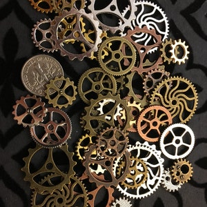 May include: A collection of gold, silver, and copper gears of various sizes and designs. The gears are arranged in a random pattern on a black background.