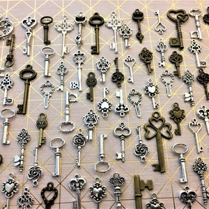 May include: A collection of antique-style skeleton keys in silver and bronze tones. The keys are arranged in a random pattern on a light pink background.