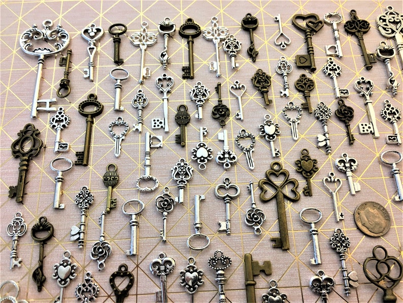 May include: A collection of antique-style skeleton keys in silver and bronze tones. The keys are arranged in a random pattern on a light pink background.
