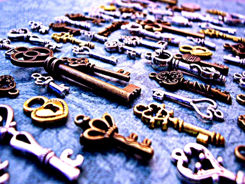 May include: A collection of antique-style skeleton keys in various sizes and finishes, including silver, gold, and bronze. The keys are scattered on a blue textured surface.