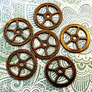 May include: Six antique gold-toned metal gears with a five-pointed star design. The gears are arranged in a circular pattern on a patterned background.