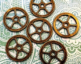 May include: Six antique gold-toned metal gears with a five-pointed star design. The gears are arranged in a circular pattern on a patterned background.