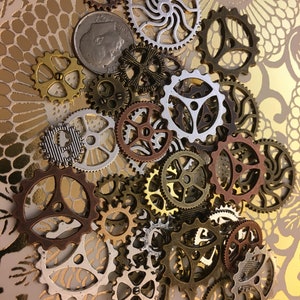 May include: A collection of assorted metal gear and cog charms in various finishes including silver, gold, bronze, and copper, featuring intricate cut-out designs and teeth, accompanied by a single silver-colored United States dime coin.