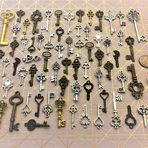 May include: A collection of antique-style skeleton keys in silver and gold tones. The keys are arranged in rows on a pink and white patterned surface.