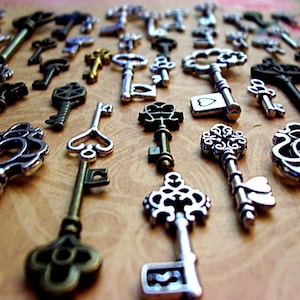 May include: A selection of antique keys in diverse designs, arranged on a light brown surface. The keys are crafted from metal and exhibit a vintage style, featuring intricate patterns and a range of colours, including silver, bronze, and gold.