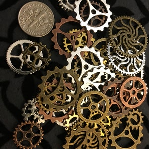 May include: A collection of assorted metal gears in various sizes and colors, including silver, gold, and bronze. The gears are arranged in a random pattern on a black background.  One US dime coin is included in the image.