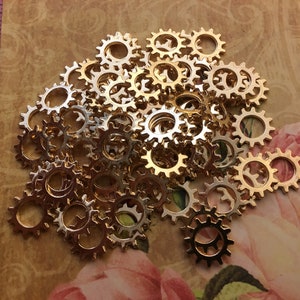 May include: A pile of gold-colored metal gears, each with a circular shape and a toothed edge. The gears are arranged in a random pattern, with some overlapping.