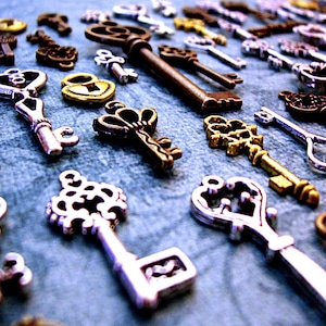 May include: A collection of antique-style keys in silver, gold, and bronze finishes. The keys feature intricate designs and are arranged on a blue surface.