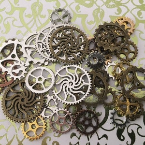 May include: A collection of various metal gears in shades of silver, bronze, and copper. The gears are of different sizes and designs, scattered on a light green and white patterned background. The gears appear to be decorative or for crafting.
