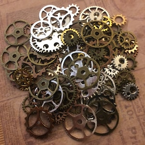 May include: A collection of various-sized metal gears in shades of bronze, silver, and gold. The gears are scattered across a brown surface, creating a steampunk or industrial aesthetic. Ideal for crafting or decorative projects.