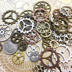 May include: A collection of various sized metal gears in shades of bronze, copper, silver, and gold. The gears are arranged on a gold and white patterned surface. The gears have different spoke designs and are a steampunk or industrial theme.
