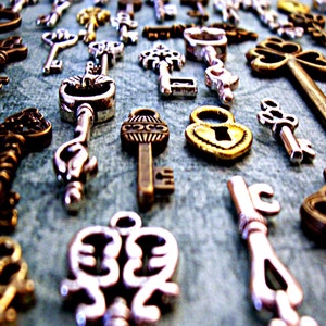May include: A collection of antique-style keys and lockets in various shades of gold and silver. The keys feature intricate designs and ornate details, including heart-shaped lockets and clover-shaped keys.