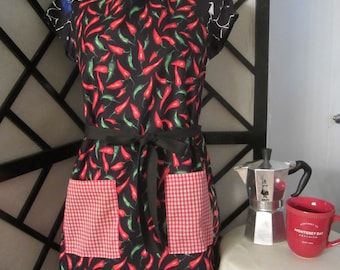May include: A black apron with a red and white checkered pocket and a chili pepper print. The apron has a black ribbon tie.