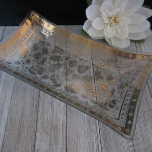 Może przedstawiać: Przezroczysta szklana taca do serwowania z pozłacanym rantem i wzorem kwiatowym. Taca leży na drewnianej powierzchni.