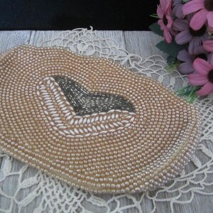 Puede incluir: Un embrague de cuentas beige con un diseño de corazón gris y blanco. El embrague está hecho de pequeñas cuentas redondas y tiene una superficie lisa y texturizada.