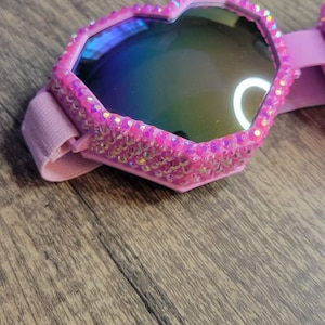 Op de afbeelding: Roze hartvormige zonnebril met iriserende glazen en een roze strassrand.