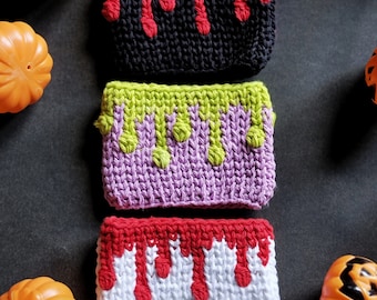 May include: Three crocheted cup cozies with a dripping blood design. The cozies are in black, purple, and white with red dripping blood accents.