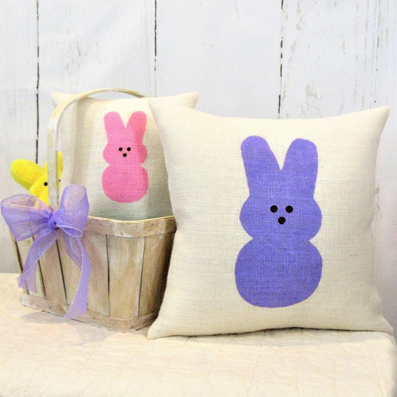May include: Two decorative throw pillows with a white background and a pink and purple bunny silhouette. The bunny silhouettes are in the shape of a Peeps candy.
