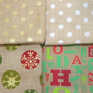 May include: Four different burlap fabric swatches with various patterns. The top left swatch has gold polka dots, the top right swatch has white polka dots, the bottom left swatch has green and red snowflakes, and the bottom right swatch has green and red letters spelling "HOLIDAY".