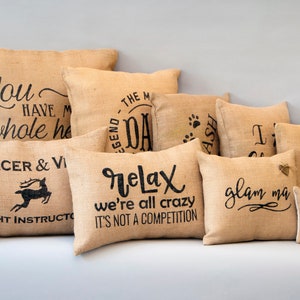 Puede incluir: Una colecci&oacute;n de 10 cojines de arpillera con diferentes lemas y dise&ntilde;os, incluyendo "You have my whole heart", "The Legend - Dad", "Prancer & Vixen - Flight Instructor", "Relax we're all crazy it's not a competition", "Glam Ma", "Grandma", y huellas de patas.